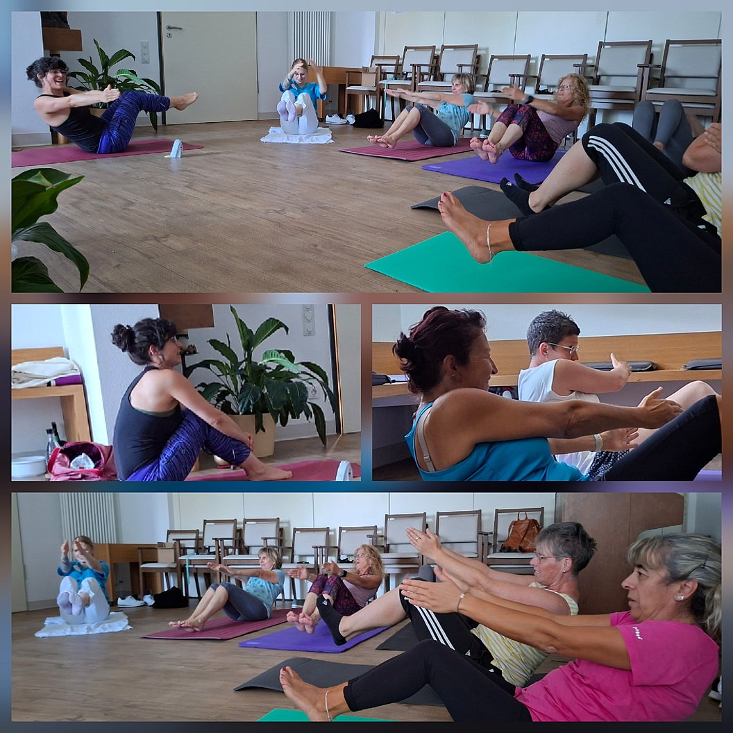 Mehrere Frauen und ein Mann machen auf Yogamatten sitzend eine Übung mit ausgestreckten Armen und angewinkelten Beinen in einem Raum mit Holzboden und Stühlen im Hintergrund